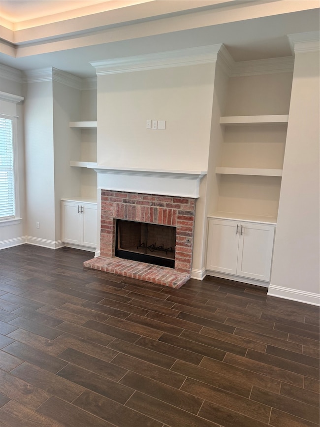 Unfurnished living room with built in shelves, a fireplace, crown molding, and dark wood-style flooring