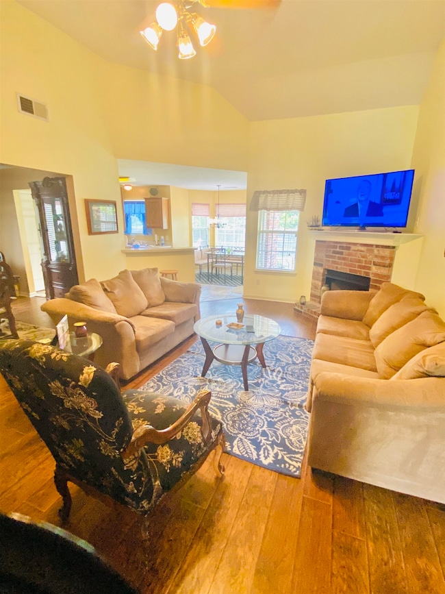 Living area with wood-type flooring, ceiling fan, a fireplace, and high vaulted ceiling