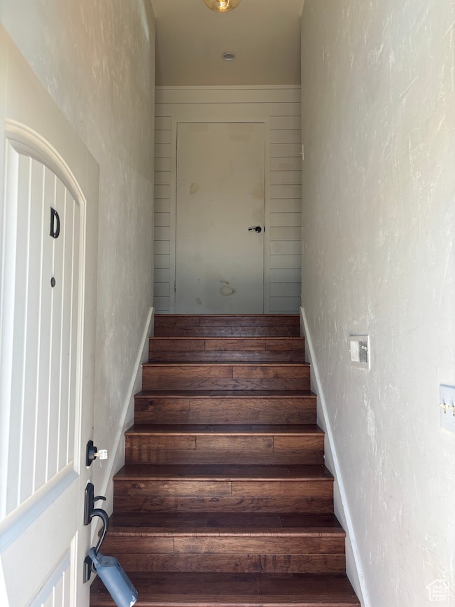 Staircase with wood finished floors and a textured wall