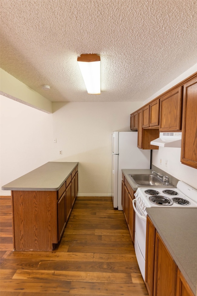 Kitchen with a peninsula, brown cabinetry, white range oven, dark wood-style flooring, and a textured ceiling