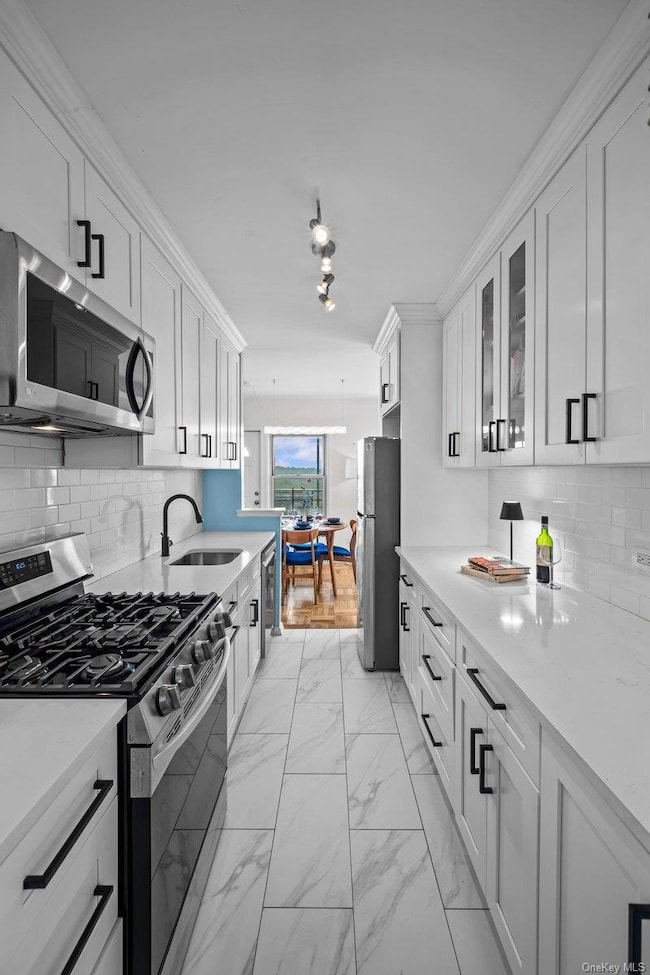 Kitchen with backsplash, light marble finish flooring, appliances with stainless steel finishes, white cabinets, and light countertops