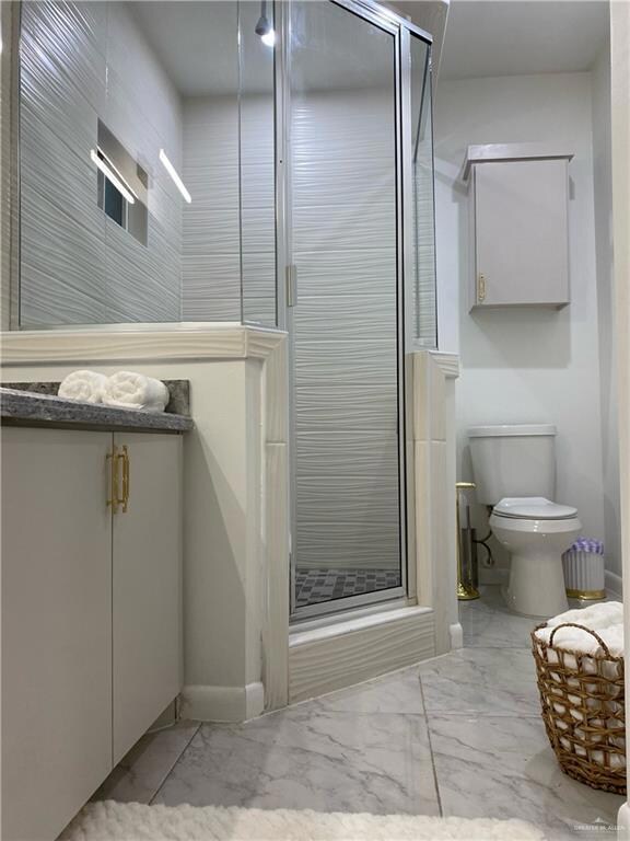 Bathroom featuring oversized vanity, toilet, tile floors, and a shower with door