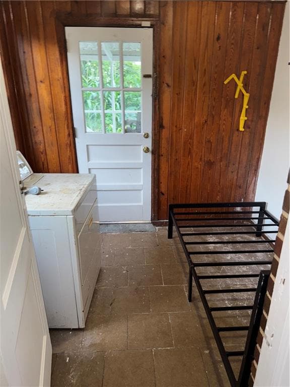 Laundry area with washer / clothes dryer, wood walls, and dark stone finish floors