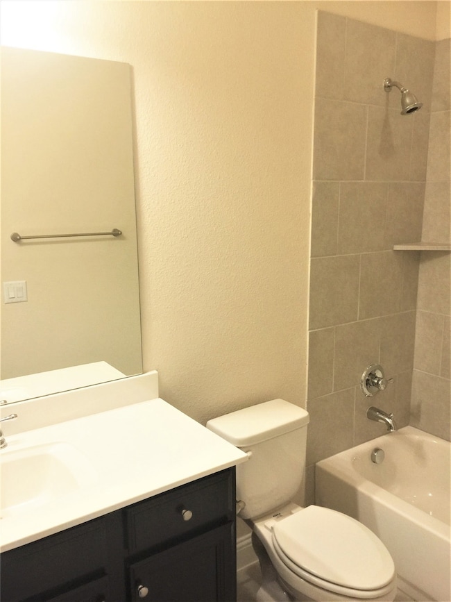 Bathroom with a textured wall, shower / bath combination, and vanity