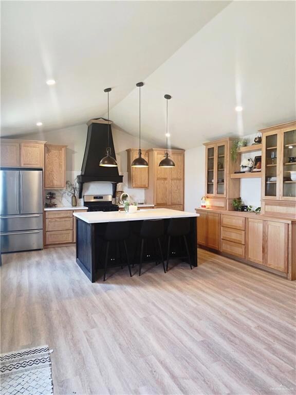 Kitchen featuring appliances with stainless steel finishes, light countertops, light wood-style floors, lofted ceiling, and glass insert cabinets