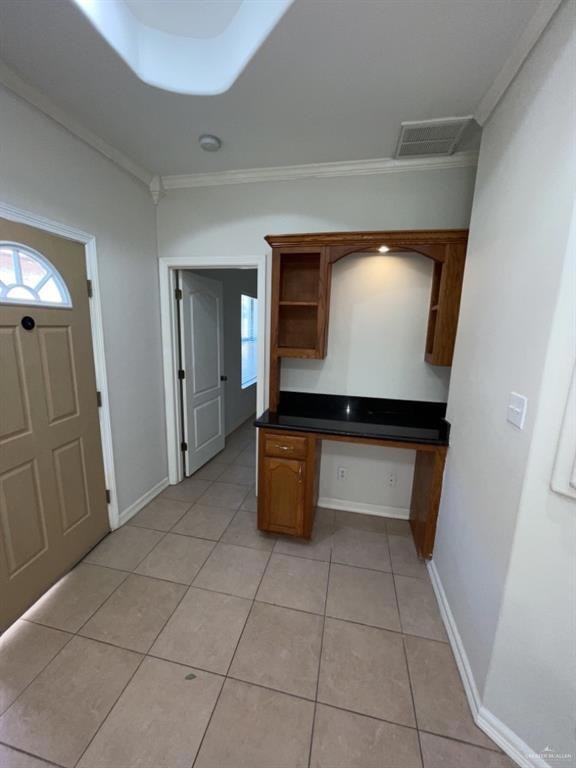 Kitchen featuring built in desk, dark countertops, brown cabinetry, light tile patterned floors, and ornamental molding
