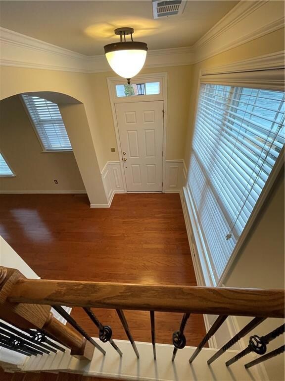 Foyer with arched walkways, dark wood finished floors, ornamental molding, and a wainscoted wall