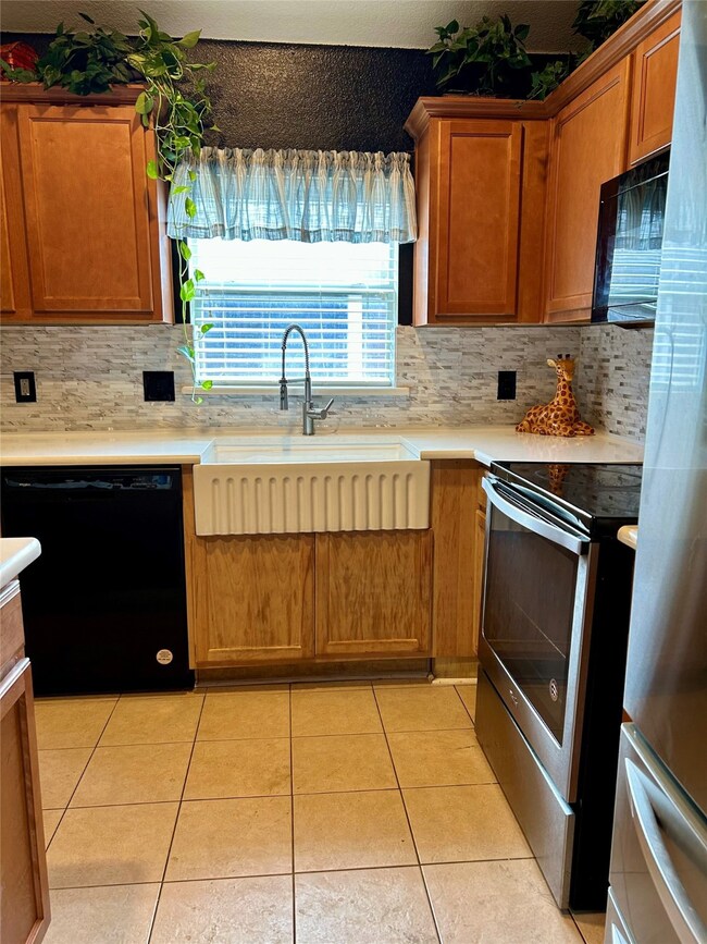 Kitchen featuring black appliances, brown cabinets, light tile patterned flooring, and backsplash