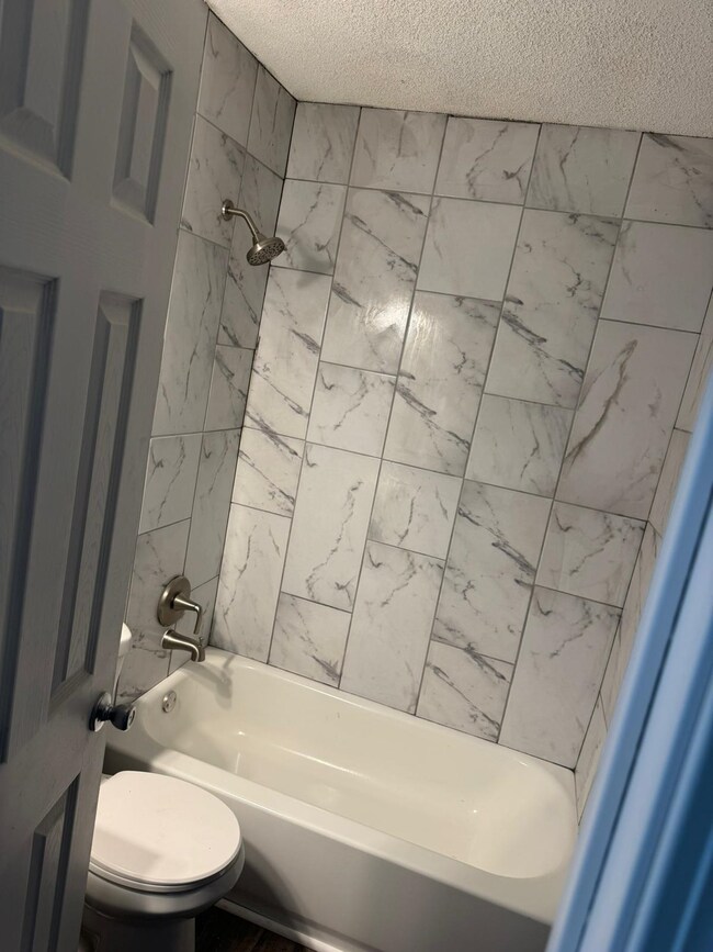Bathroom featuring a textured ceiling, shower / tub combination, and toilet