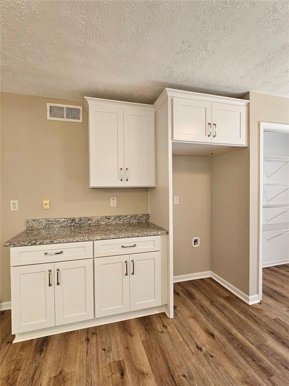 Kitchen with light stone counters, white cabinetry, dark wood-type flooring, and a textured ceiling