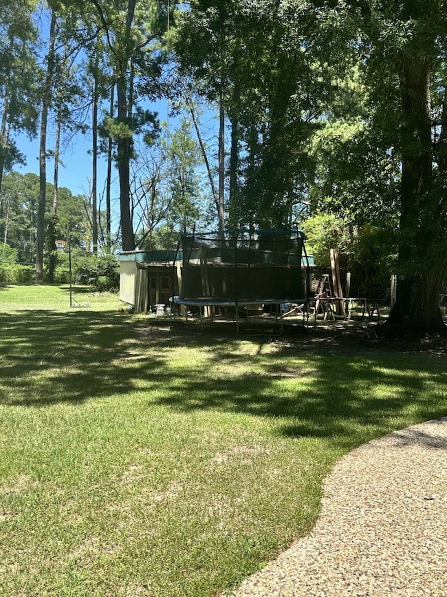 View of grassy yard with a trampoline and view of scattered trees