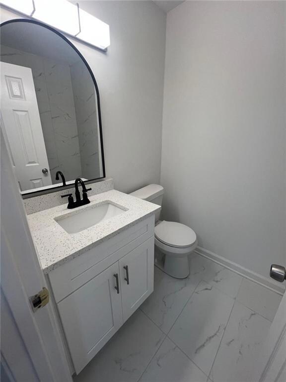 Bathroom with marble look tiles, vanity, toilet, and baseboards
