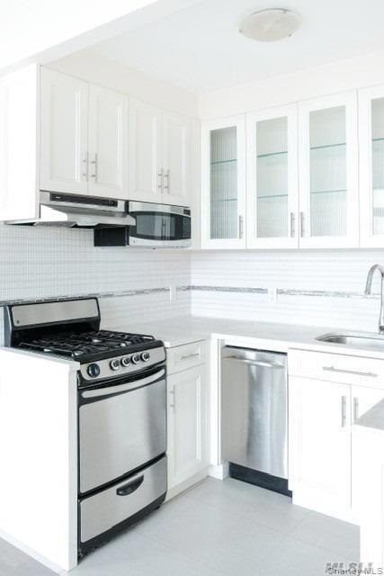 Kitchen with white cabinets, stainless steel appliances, tasteful backsplash, glass insert cabinets, and under cabinet range hood