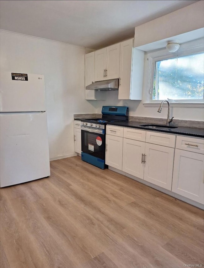 Kitchen featuring freestanding refrigerator, dark countertops, stainless steel gas range, white cabinets, and light wood finished floors