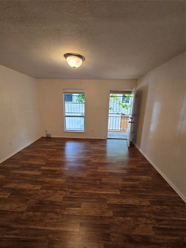 Unfurnished room with a textured ceiling, healthy amount of natural light, and dark wood-style floors