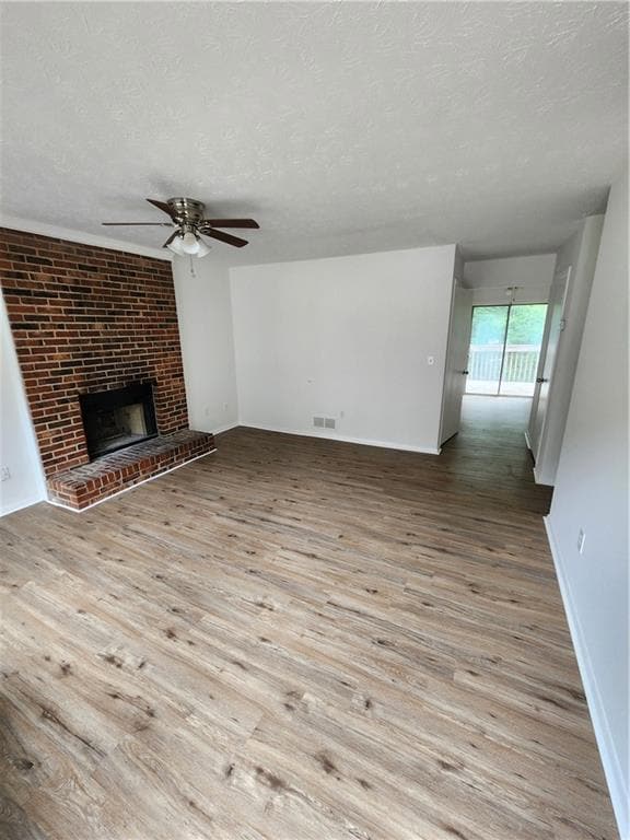 Unfurnished living room featuring ceiling fan, a textured ceiling, wood finished floors, baseboards, and a fireplace