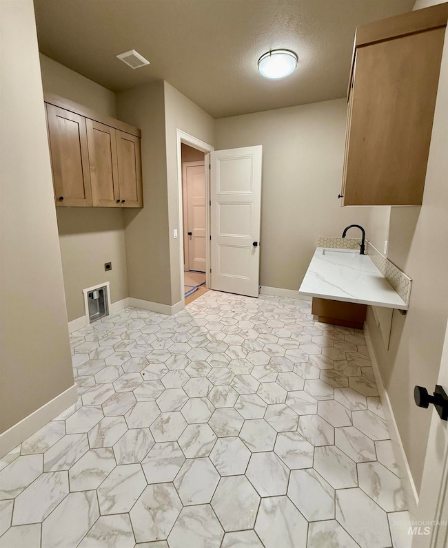 Laundry room with hookup for an electric dryer, cabinet space, and a textured ceiling