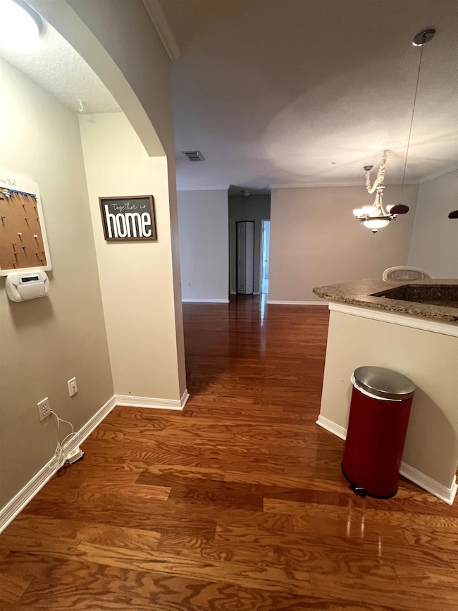Hallway with arched walkways, dark wood-style floors, and ornamental molding