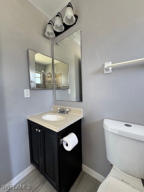 Bathroom with baseboards, vanity, toilet, and wood