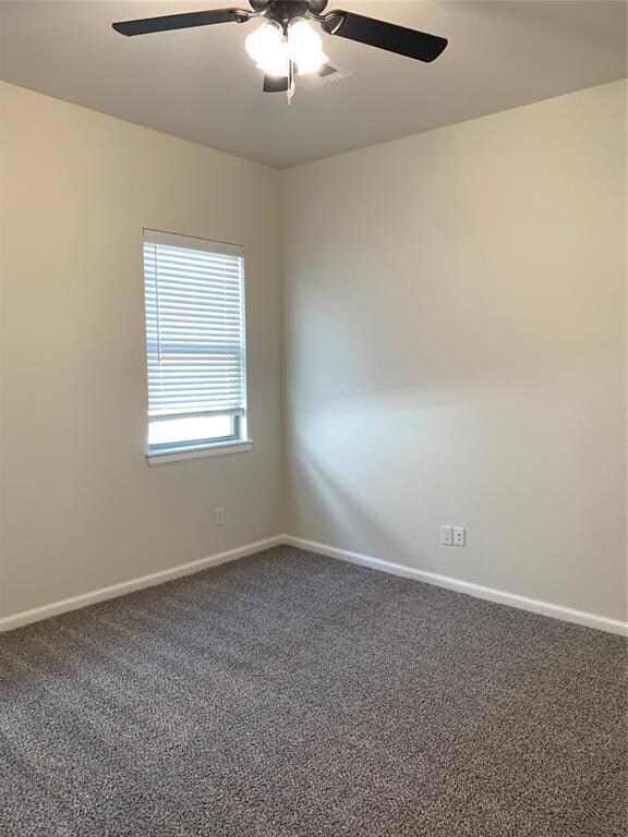 Carpeted empty room featuring ceiling fan and base