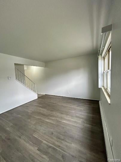 Spare room featuring dark wood-type flooring, a baseboard radiator, and stairway