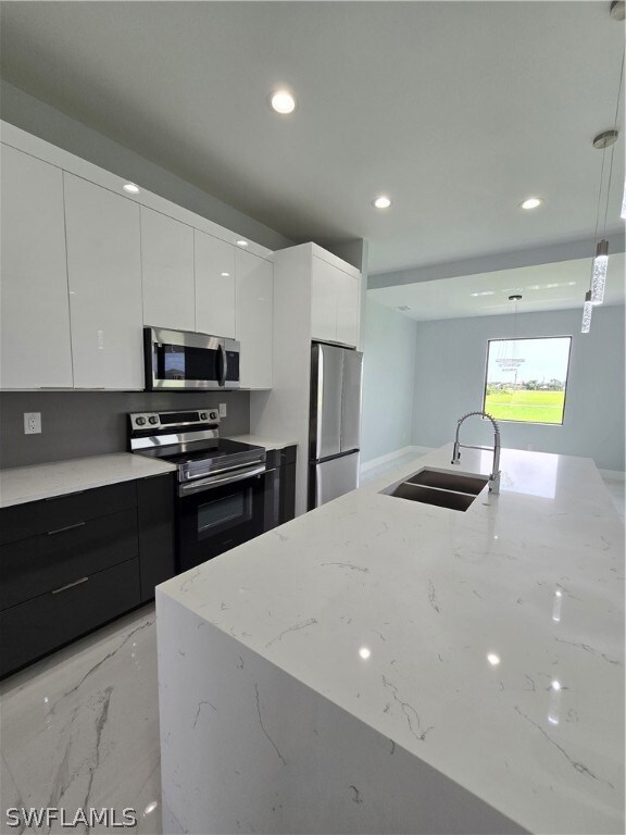 Kitchen featuring pendant lighting, stove, sink, white cabinets, and stainless steel refrigerator