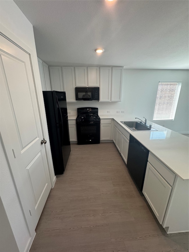 Kitchen with light countertops, a peninsula, black appliances, white cabinets, and a textured ceiling