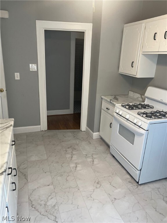 Kitchen featuring light tile floors, white gas range oven, and white cabinetry