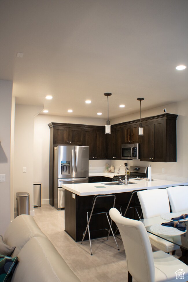 Kitchen featuring stainless steel appliances, recessed lighting, a kitchen breakfast bar, dark brown cabinetry, and light countertops