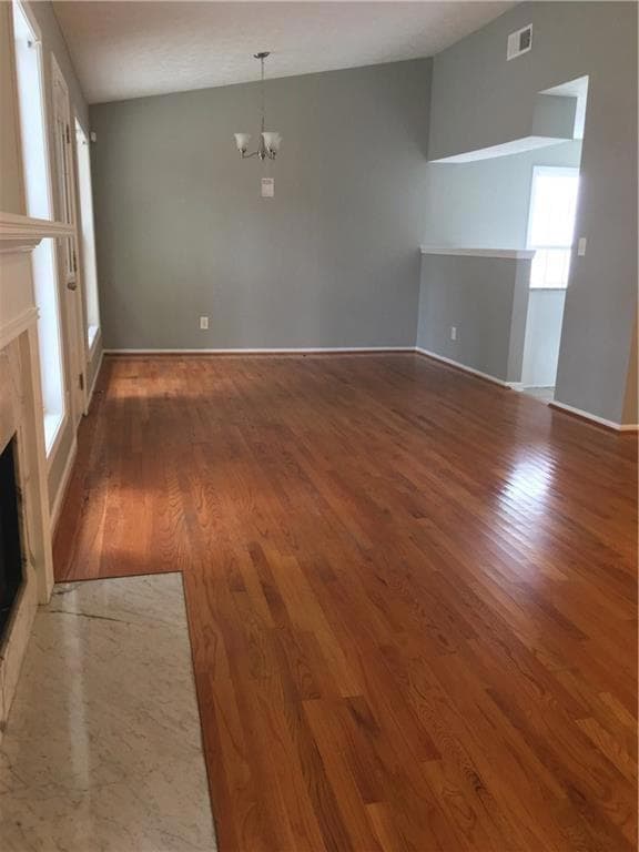 Unfurnished living room with a fireplace, a chandelier, wood finished floors, and baseboards
