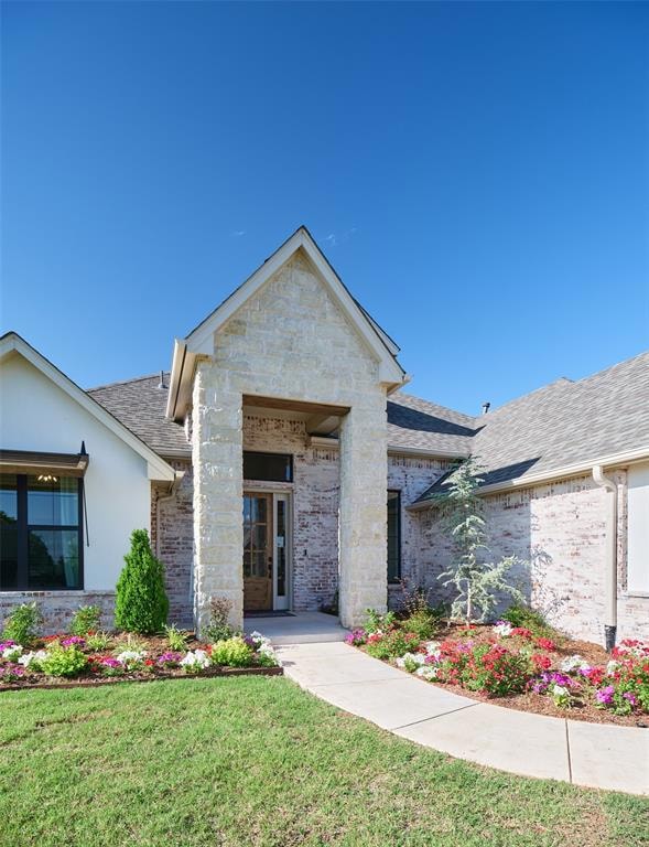 View of front of house with roof with shingles, a front yard, brick siding, and stone siding