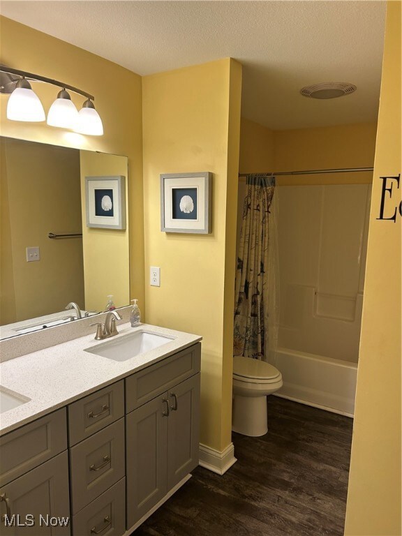 Bathroom featuring a textured ceiling, a sink, toilet, and wood finished floors