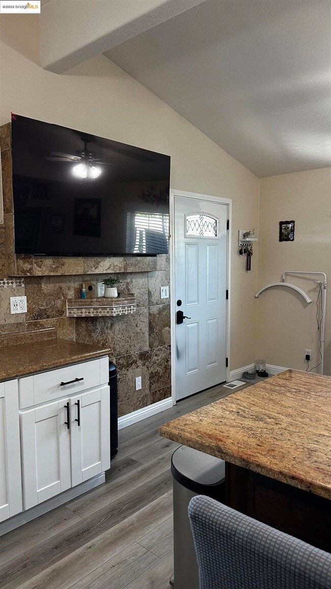 Kitchen featuring lofted ceiling, light wood finished floors, white cabinetry, ceiling fan, and dark stone counters