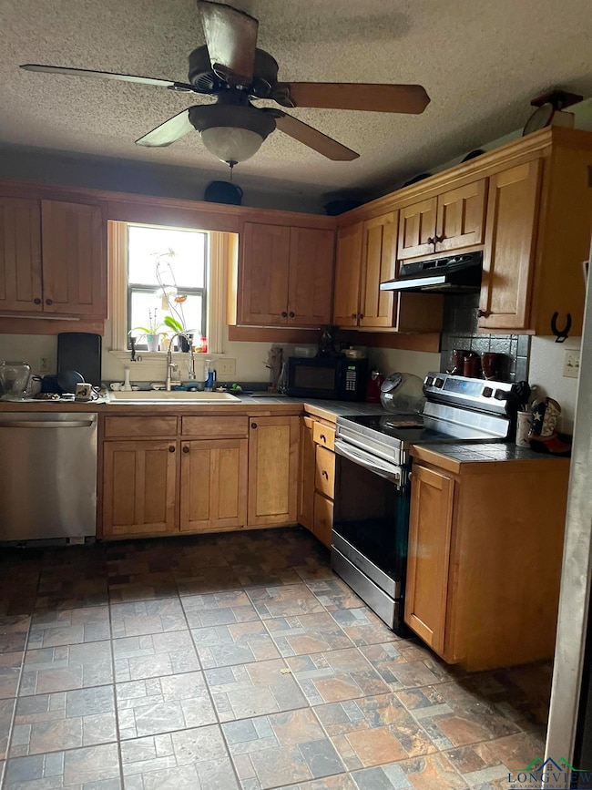 Kitchen featuring stainless steel appliances, under cabinet range hood, a sink, a ceiling fan, and a textured ceiling