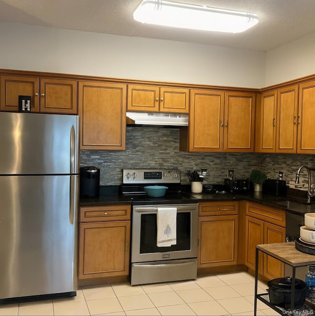 Kitchen featuring stainless steel appliances, brown cabinetry, decorative backsplash, light tile patterned floors, and a textured ceiling