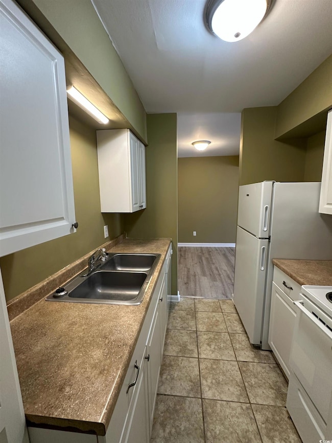 Kitchen with white cabinetry, sink, light tile pat
