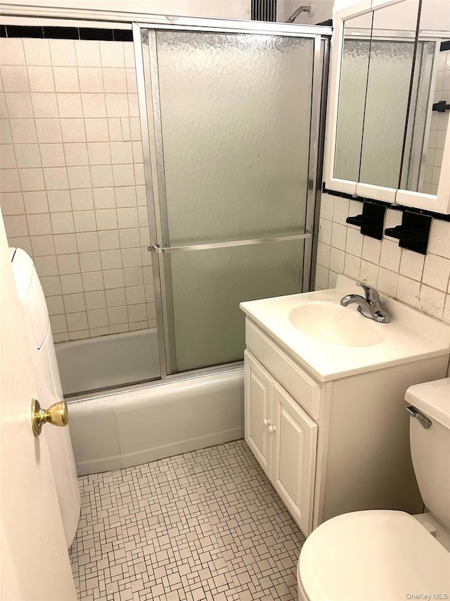 Bathroom featuring combined bath / shower with glass door, vanity, and tile walls