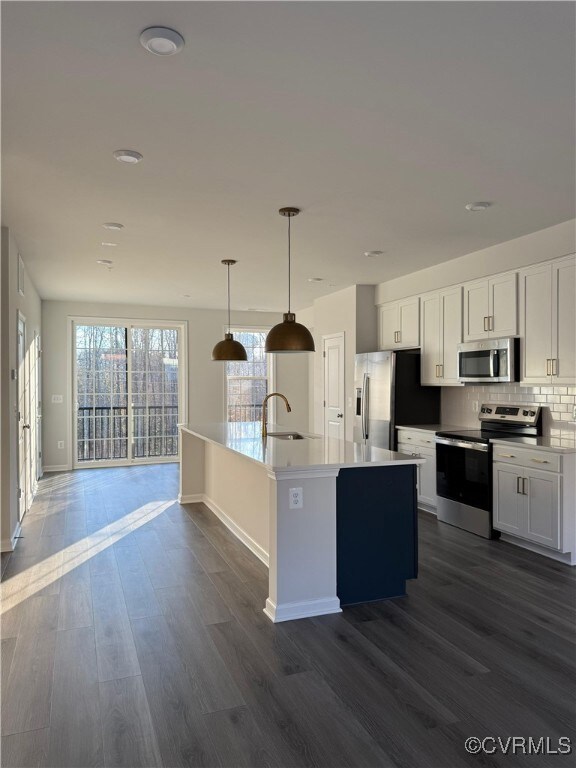 Kitchen featuring appliances with stainless steel finishes, dark hardwood / wood-style floors, white cabinetry, and hanging light fixtures