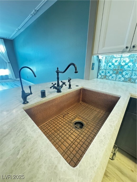 Kitchen view of a sink, white cabinetry, and light