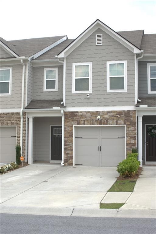 Townhome / multi-family property featuring stone siding, concrete driveway, a shingled roof, and an attached garage
