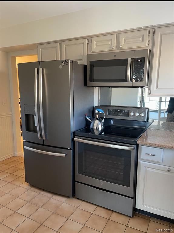 Kitchen with stainless steel appliances, light tile patterned floors, light stone counters, and a wainscoted wall
