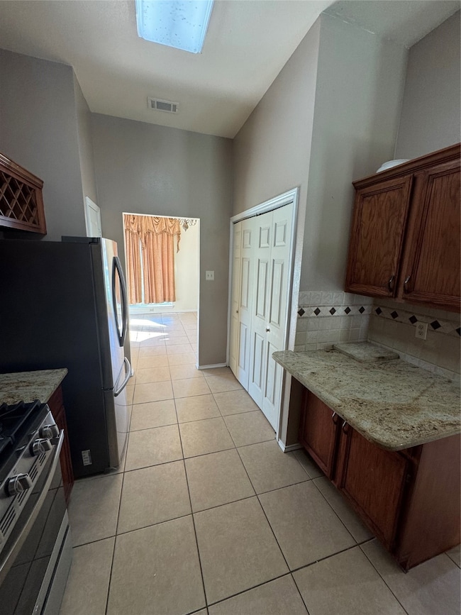 Kitchen featuring range, light stone countertops, light tile patterned floors, and brown cabinets