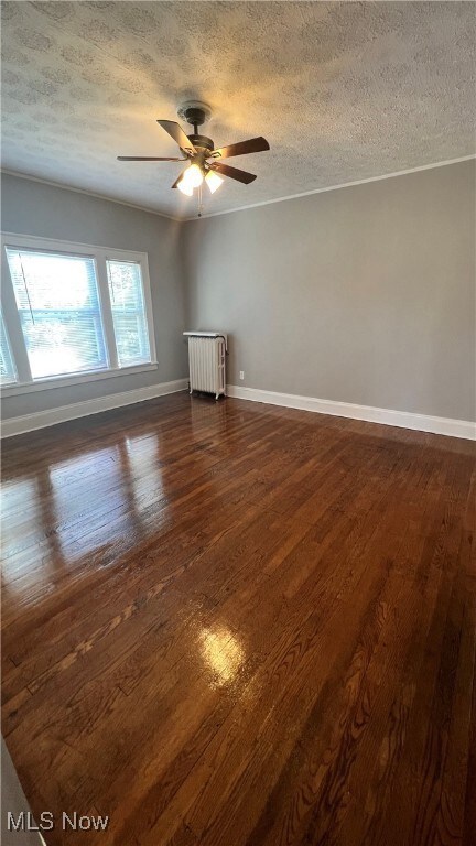 Empty room with a textured ceiling, dark wood-style floors, radiator heating unit, and a ceiling fan