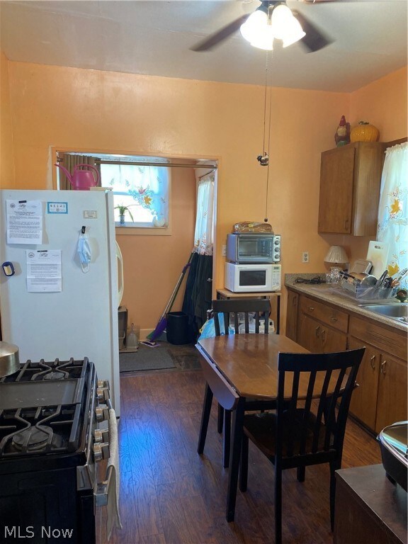 Kitchen with hanging light fixtures, dark wood-type flooring, stove, sink, and ceiling fan
