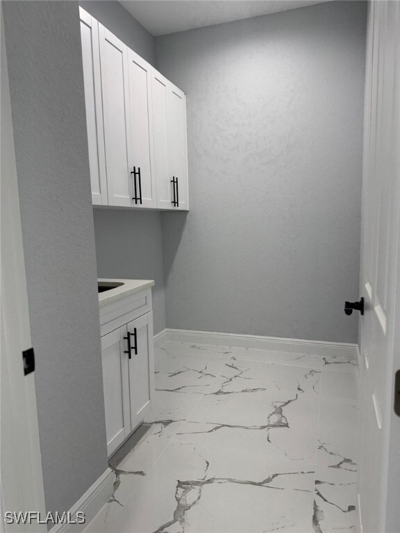 Laundry area with baseboards and light marble fini