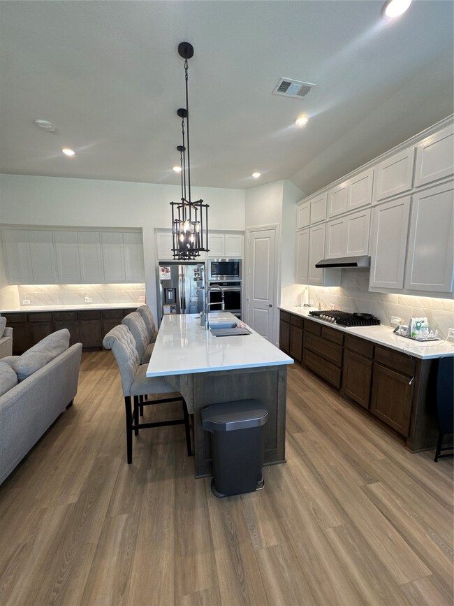 Kitchen featuring a breakfast bar area, decorative light fixtures, white cabinetry, an island with sink, and backsplash