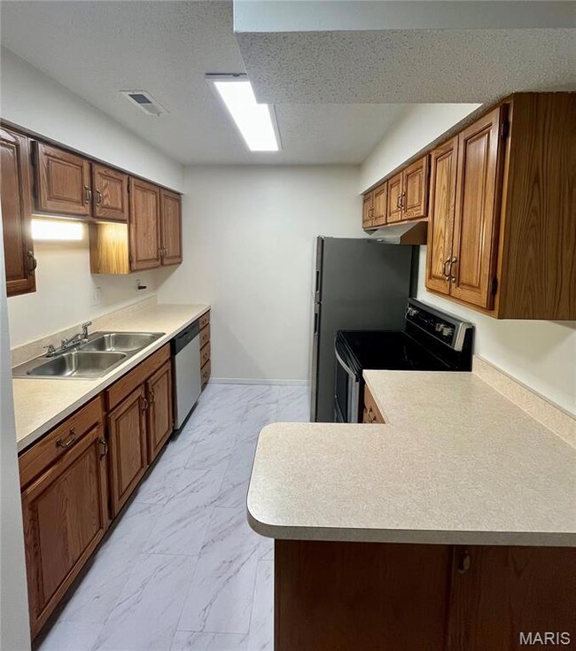 Kitchen featuring appliances with stainless steel finishes, brown cabinets, light marble finish floors, light countertops, and a textured ceiling