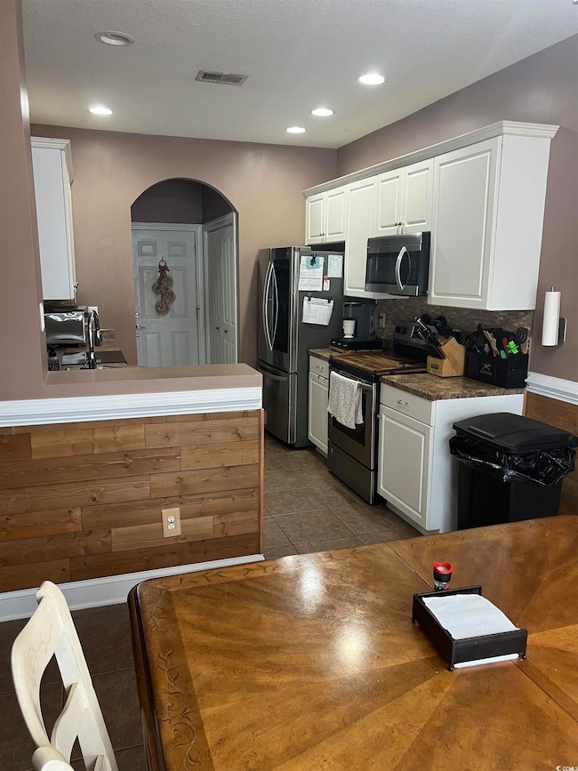 Kitchen with white cabinetry, appliances with stai