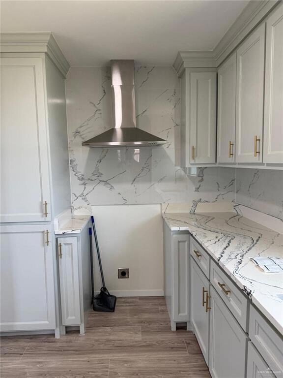 Kitchen featuring wall chimney range hood, light stone counters, and light wood-type flooring