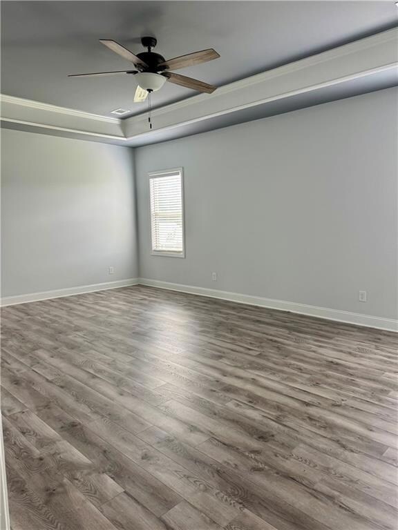 Empty room with wood finished floors, ceiling fan, baseboards, and a tray ceiling